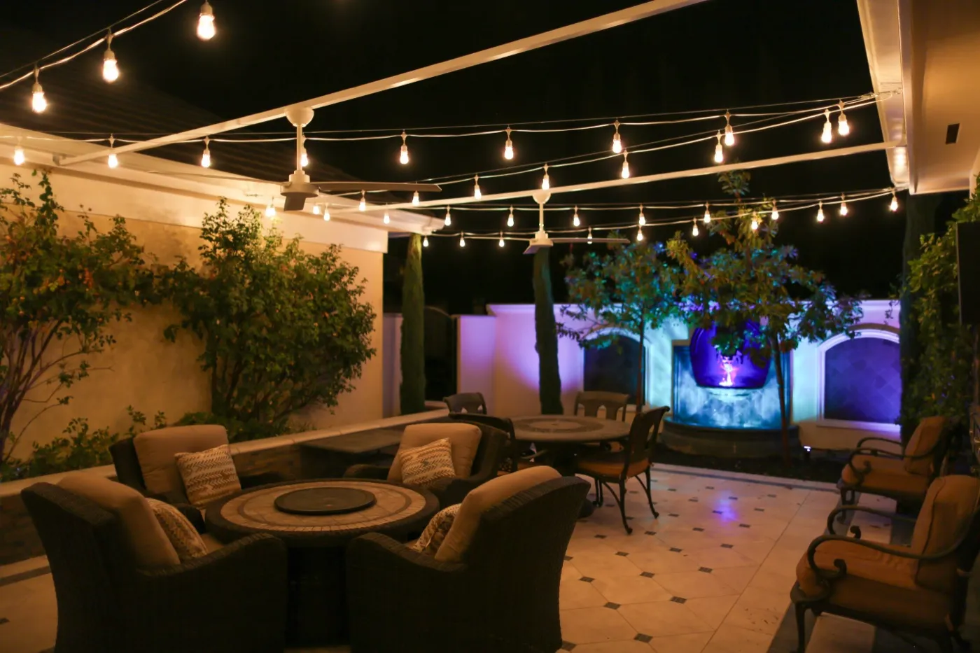 Patio seating area with uplit trees, washed walls, and a lit water feature