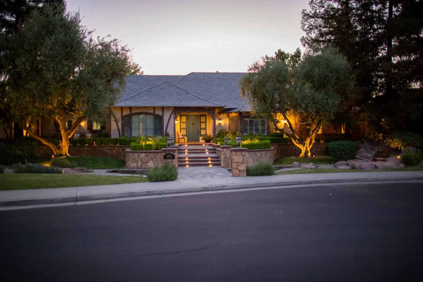 Bakersfield home with illuminated olive trees, entry steps, and front elevation