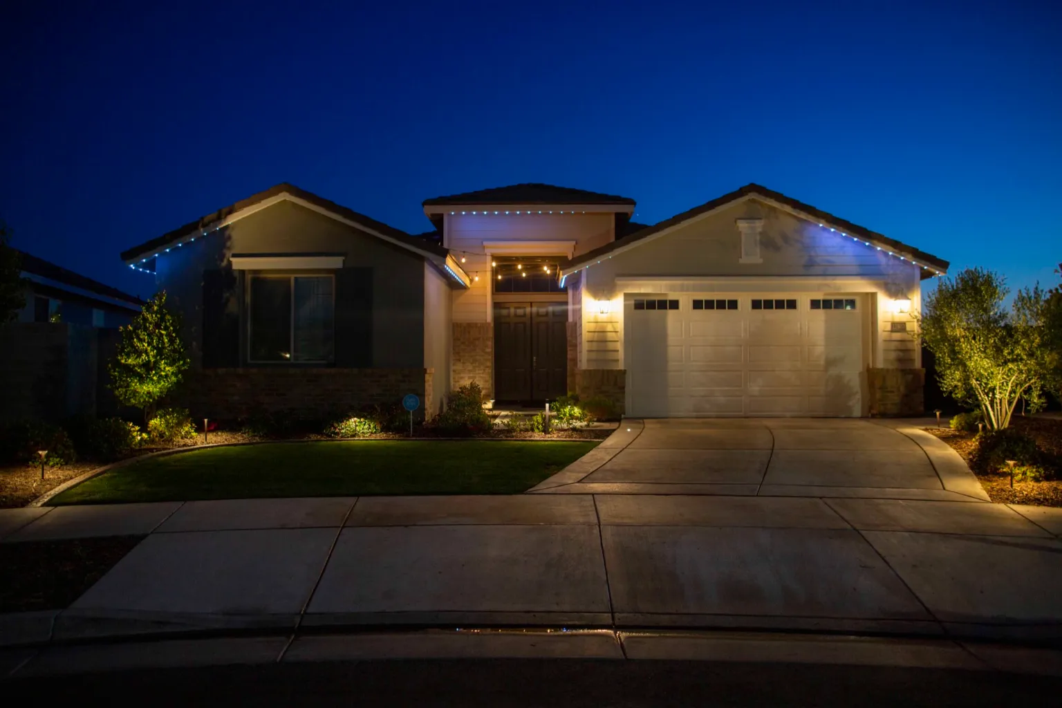 Warm architectural uplighting across a Bakersfield home, garage, and front landscaping